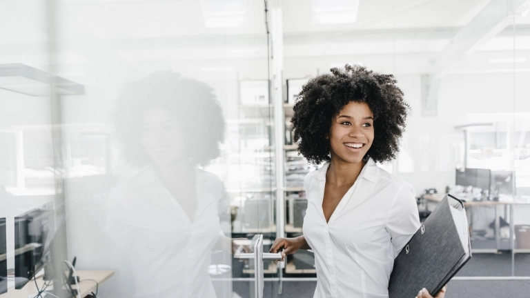 Junge Frau mit Lockenfrisur im Büro mit einem Leitzordner unter dem Arm